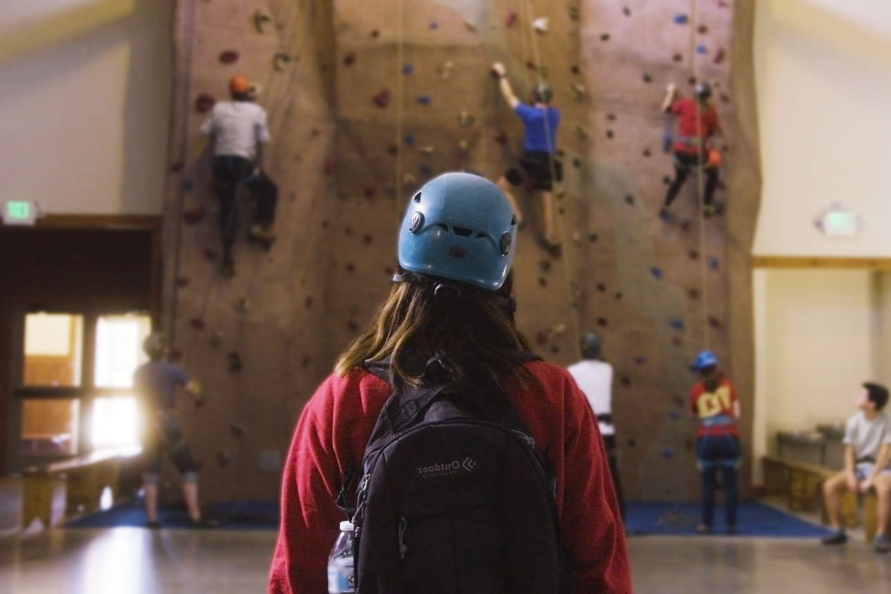 student, from back, in front of climbing wall